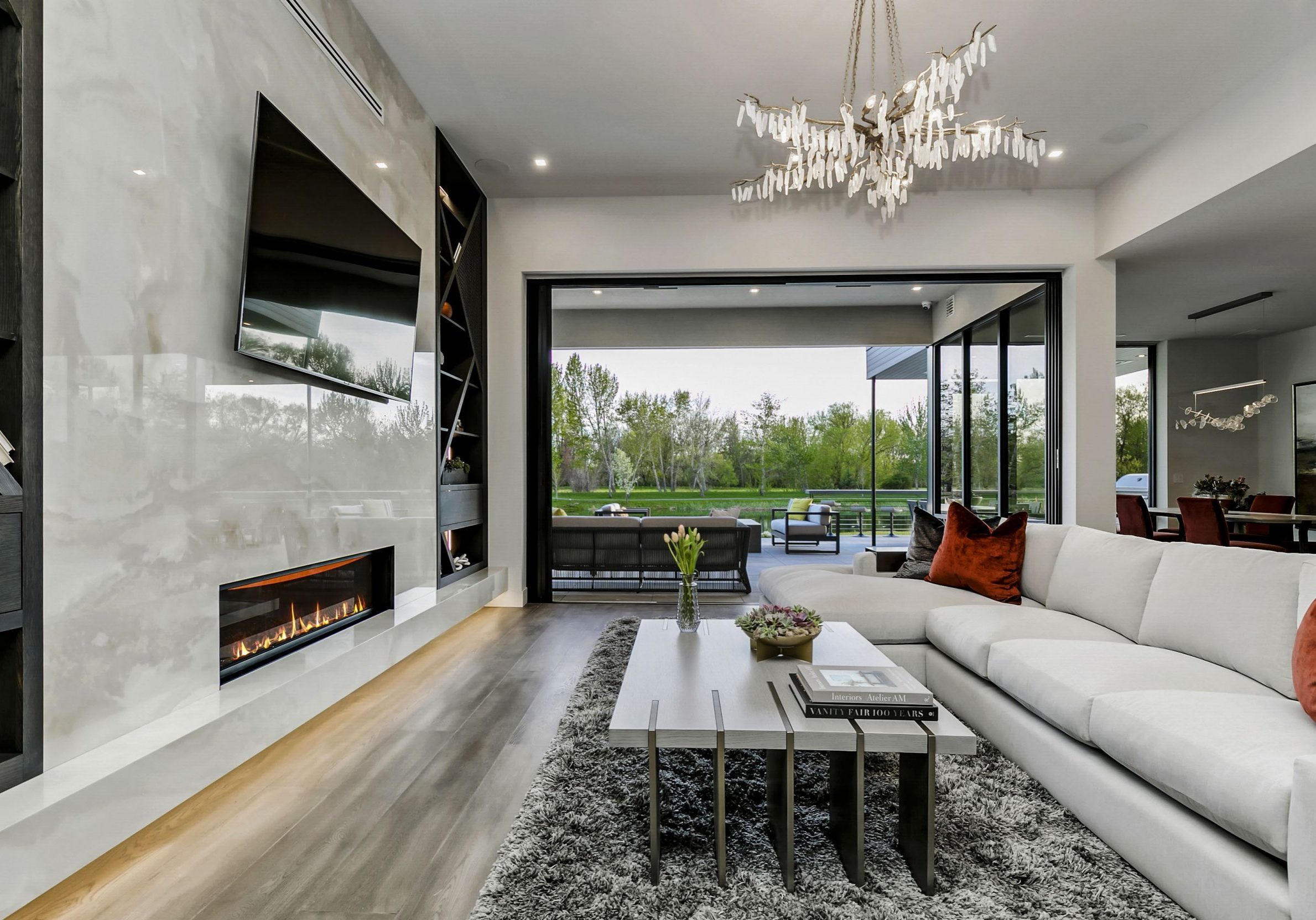 Modern living room with high contrast detail, light gray marble fireplace with built in shelving. Open sliding glass doors reveal a luxurious back patio with views of the water at Renovare in Eagle, Idaho