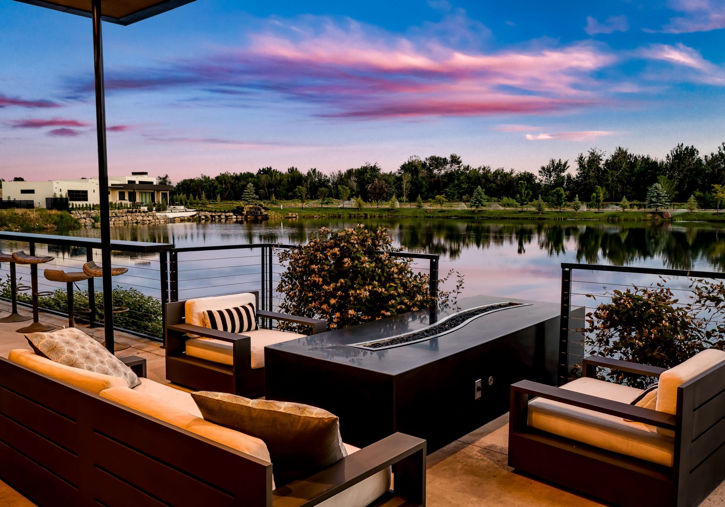 Outdoor couches and firepit table overlooking the water at Renovare in Eagle. Sunset sky and lush landscpaing reflect off the water